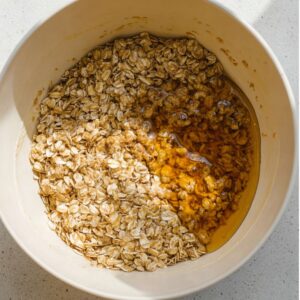 Easy Granola Recipe: Crunchy Clusters in Just 30 Minutes 17 Overhead close-up of rolled oats mixed with honey and oil in a large white bowl, sticky texture, natural light, minimal food styling, homemade granola preparation, realistic food photography