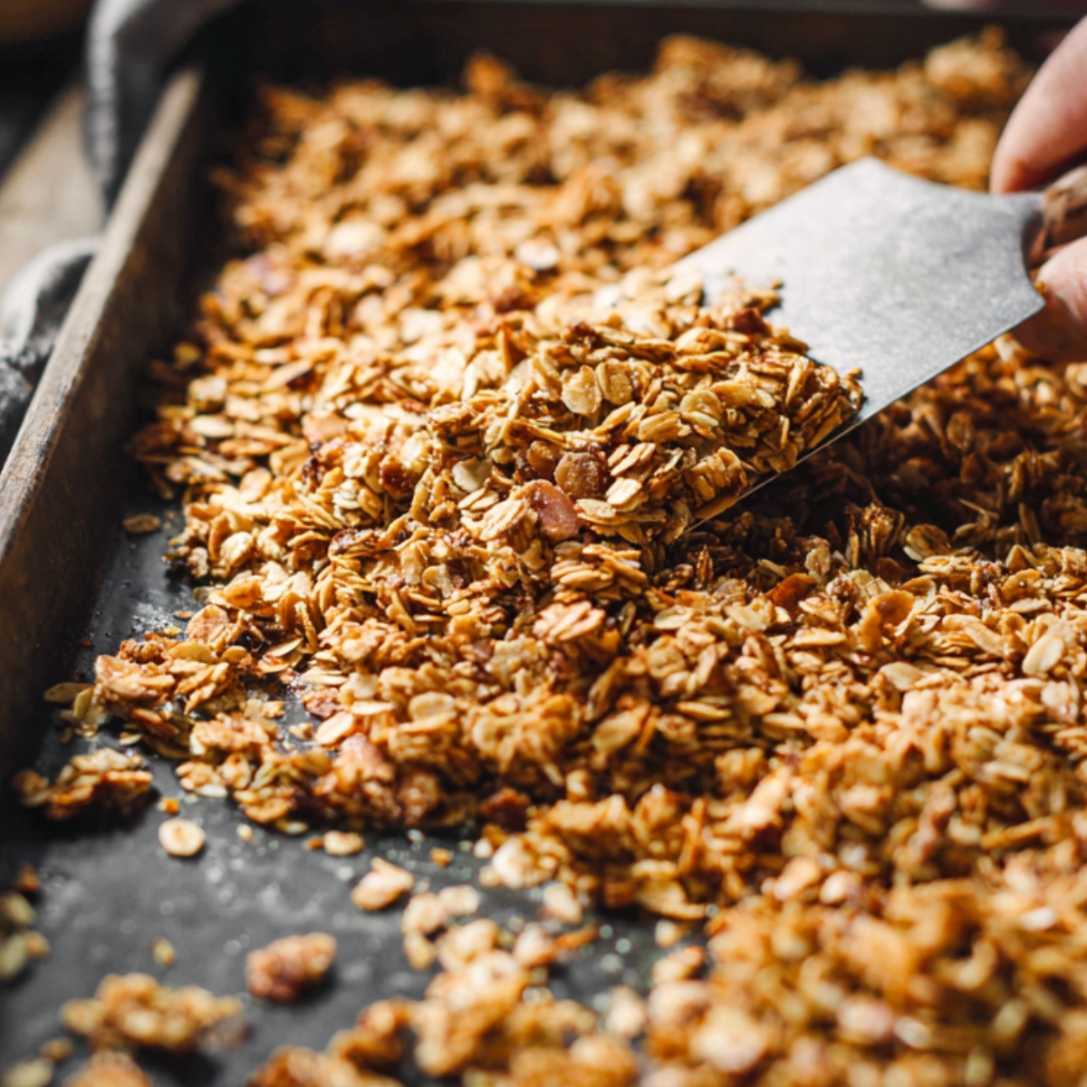 Easy Granola Recipe: Crunchy Clusters in Just 30 Minutes 13 Freshly baked granola on a baking sheet being cut into clusters with a spatula, golden brown oats and nuts, crunchy texture, rustic kitchen setting, natural light, high-detail food photography