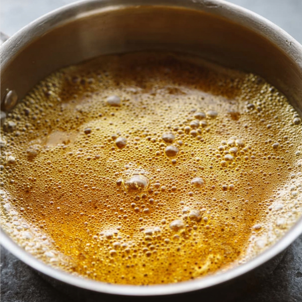 Easy Granola Recipe: Crunchy Clusters in Just 30 Minutes 11 Close-up of honey and oil mixture gently bubbling in a small saucepan, golden color, smooth texture, minimal kitchen background, natural soft lighting, realistic cooking photography