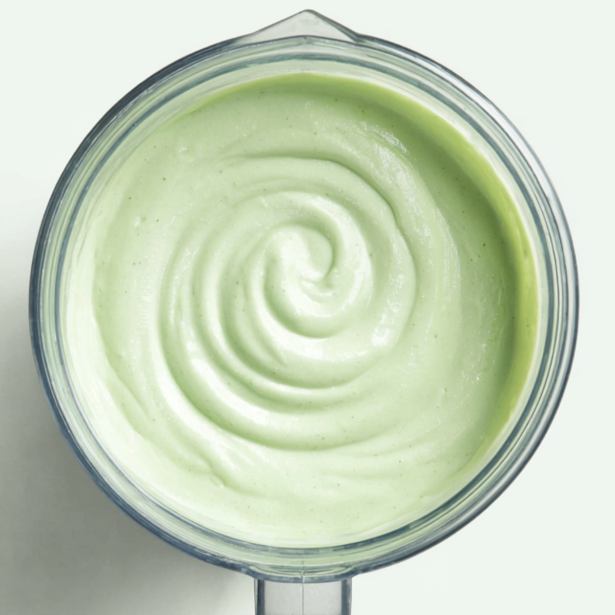 Grasshopper Drink Recipe | 4-Ingredient Frozen Cocktail 10 Top-down view of a blender jar containing a creamy pale green mint drink with a smooth spiral on the surface.