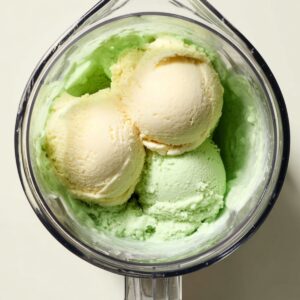 Grasshopper Drink Recipe | 4-Ingredient Frozen Cocktail 16 Overhead view of vanilla ice cream scoops added to a pale green mint mixture inside a blender jar.