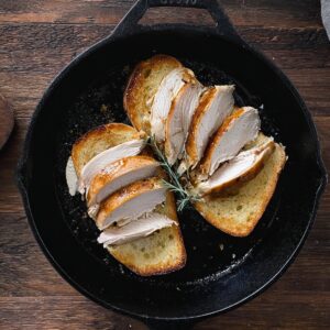 Kentucky Hot Brown Recipe - Easy & Ready in 30 Minutes 15 Overhead view of sliced roasted turkey arranged on toasted bread in a cast iron skillet on a rustic wooden surface