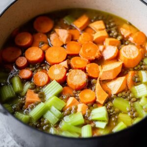 Best Lebanese Lentil Soup Recipe (Healthy & So Comforting!) 15 A close-up of fresh ingredients for Lebanese lentil soup, including sliced carrots, sweet potatoes, and celery in a pot.