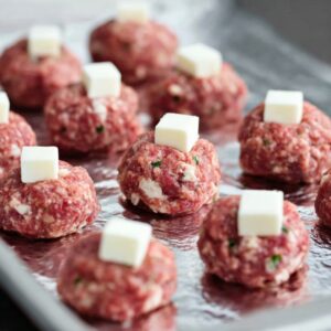 Easy Mozzarella Stuffed Meatballs | 8 Simple Steps (55 characters) 17 Raw beef meatballs stuffed with mozzarella cubes, arranged neatly on a foil-lined baking sheet, clean kitchen background, soft natural lighting, close-up food photography, high realism, ultra detailed