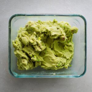 Easy Pistachio Cookie Bars | 40-Minute Dessert Recipe 15 Overhead shot of raw pistachio cookie dough placed in a glass baking dish, chunky uneven texture, vibrant pistachio-green color, neutral stone countertop, natural light, authentic homemade baking preparation photography.