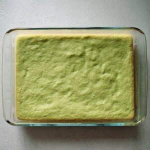 Easy Pistachio Cookie Bars | 40-Minute Dessert Recipe 16 Top-down view of baked pistachio cookie base in a glass baking dish, light green color with soft pillowy texture, slightly golden edges, minimalistic background, realistic baking process photo, natural daylight.