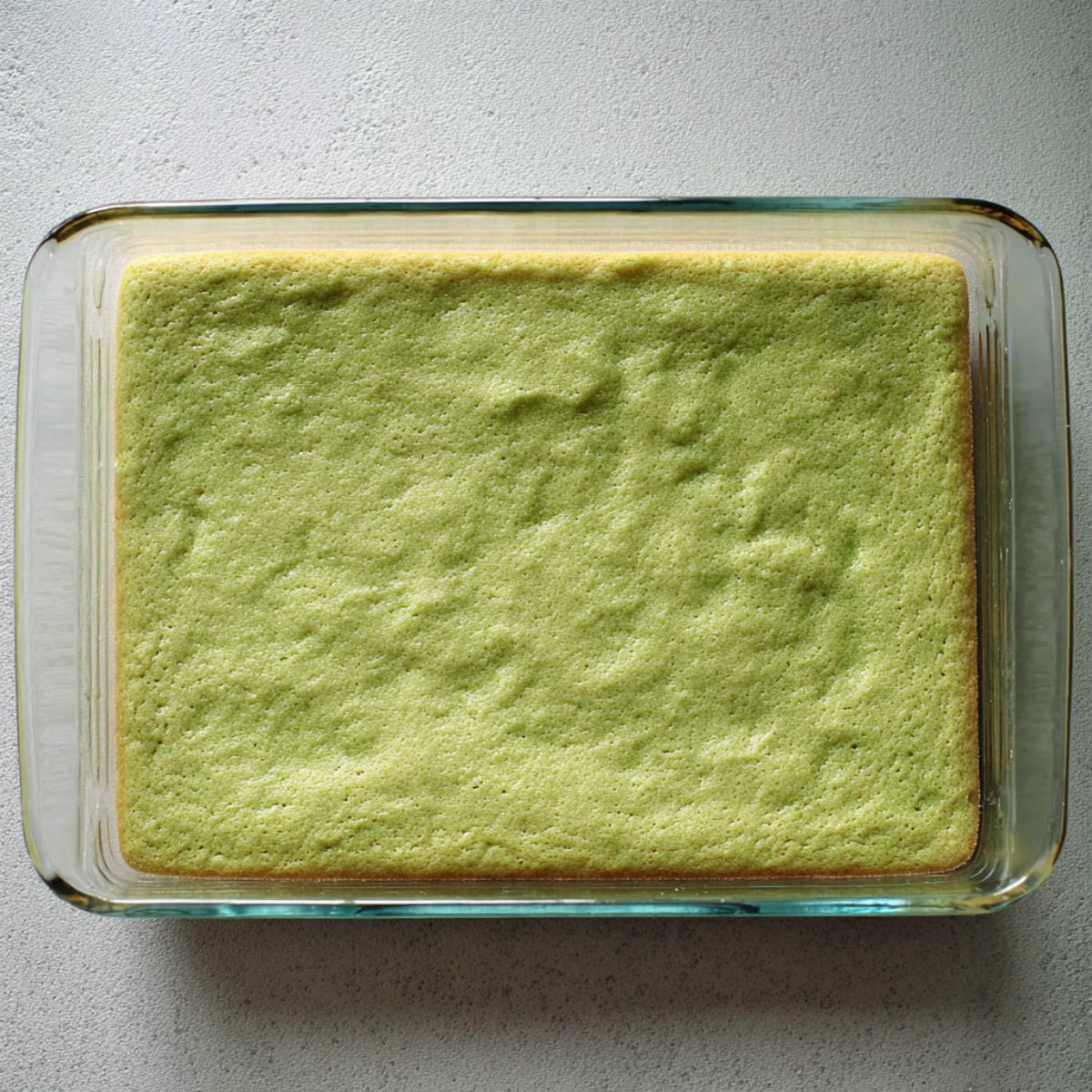 Easy Pistachio Cookie Bars | 40-Minute Dessert Recipe 11 Top-down view of baked pistachio cookie base in a glass baking dish, light green color with soft pillowy texture, slightly golden edges, minimalistic background, realistic baking process photo, natural daylight.