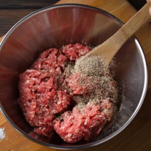 Smash Burger Tacos Recipe | Crispy & Easy in Minutes 16 A bowl of ground beef being seasoned with salt and pepper, ready to be mixed and shaped into patties for cooking smash burgers.