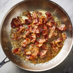 Easy Spaghetti Carbonara Recipe 15 Crispy bacon pieces cooking in a stainless steel skillet with rendered fat.