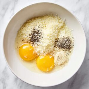 Easy Spaghetti Carbonara Recipe 16 Raw eggs with grated parmesan cheese and black pepper in a white bowl for carbonara sauce.