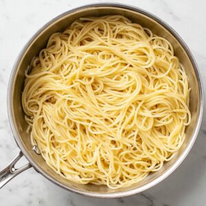Easy Spaghetti Carbonara Recipe 17 Cooked spaghetti noodles in a stainless steel pot on a marble countertop.