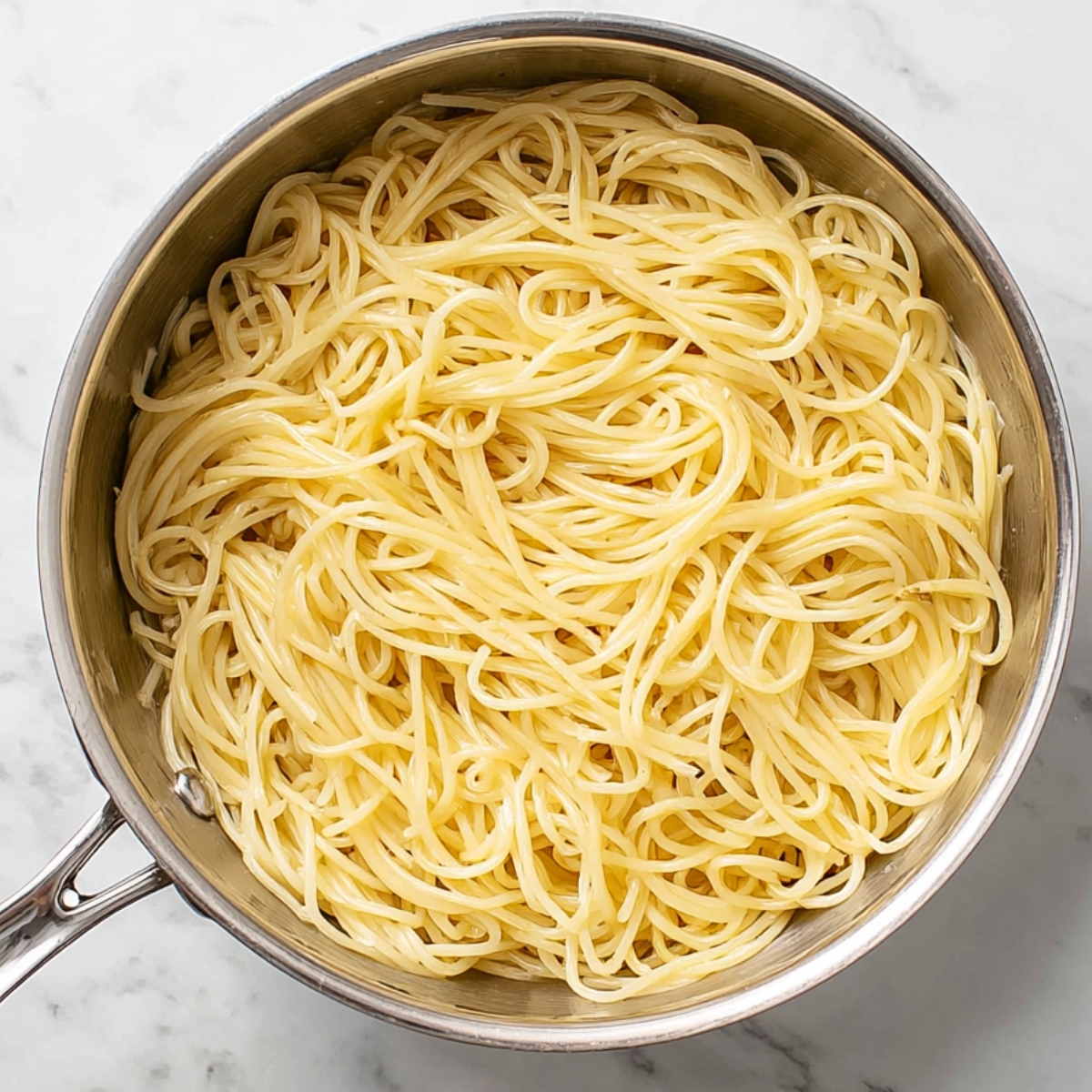Easy Spaghetti Carbonara Recipe 12 Cooked spaghetti noodles in a stainless steel pot on a marble countertop.