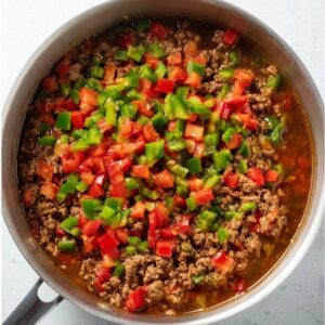 Stuffed Pepper Soup Recipe | Easy & Comforting in 52 Min 15 Top-down view of browned ground beef in a pot topped with freshly chopped red and green bell peppers, vibrant colors, meal prep stage, clean composition, realistic food photography, bright natural lighting