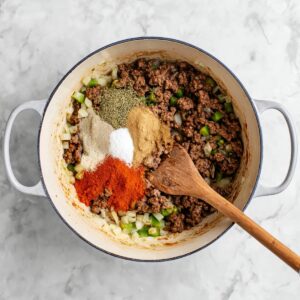 One-Pan Taco Spaghetti Recipe | Ready in 30 Minutes 16 Browned ground beef with onions and green peppers in a pot, topped with taco seasoning spices before mixing.