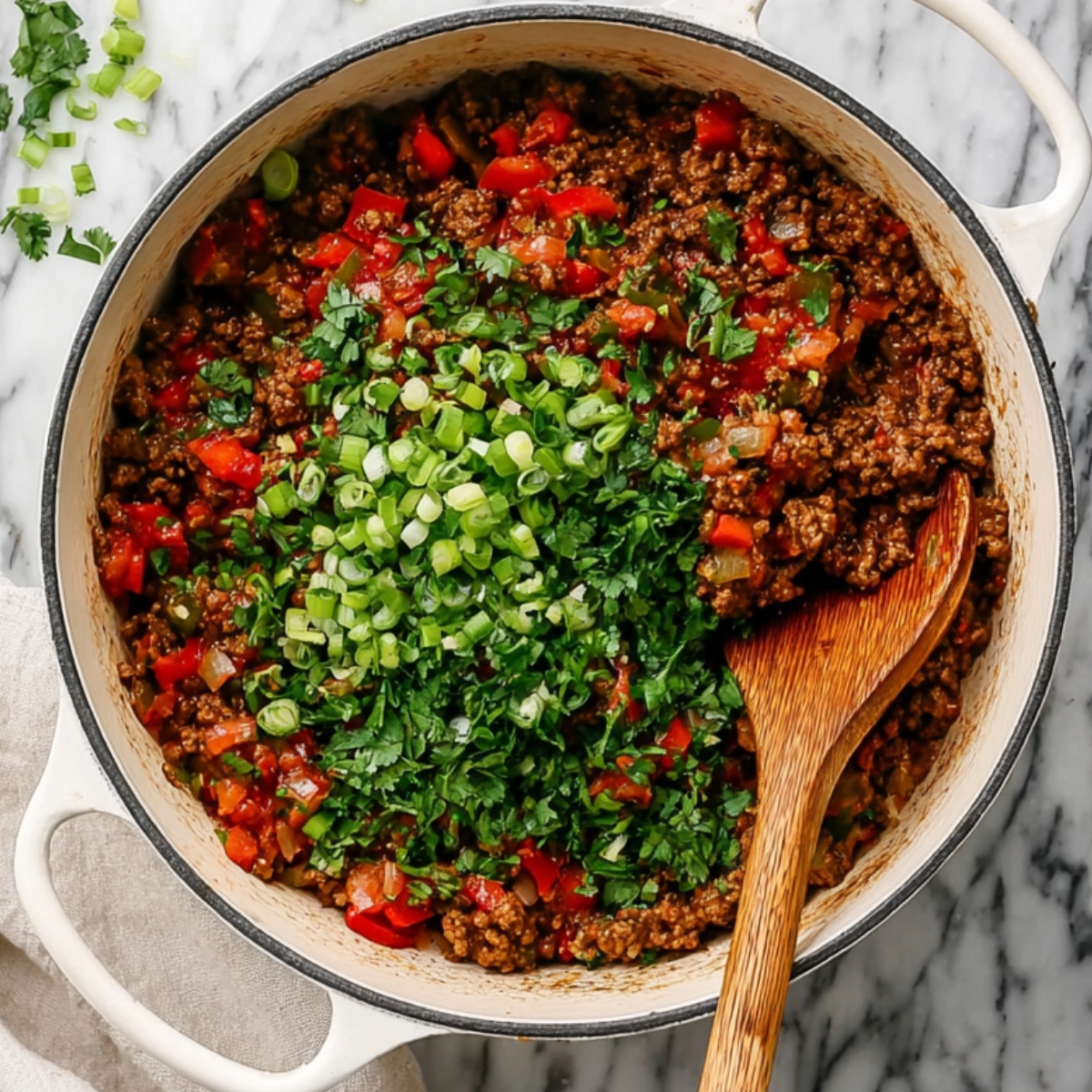 One-Pan Taco Spaghetti Recipe | Ready in 30 Minutes 12 Cooked taco-seasoned ground beef with tomatoes and onions in a pot, topped with fresh cilantro and green onions.