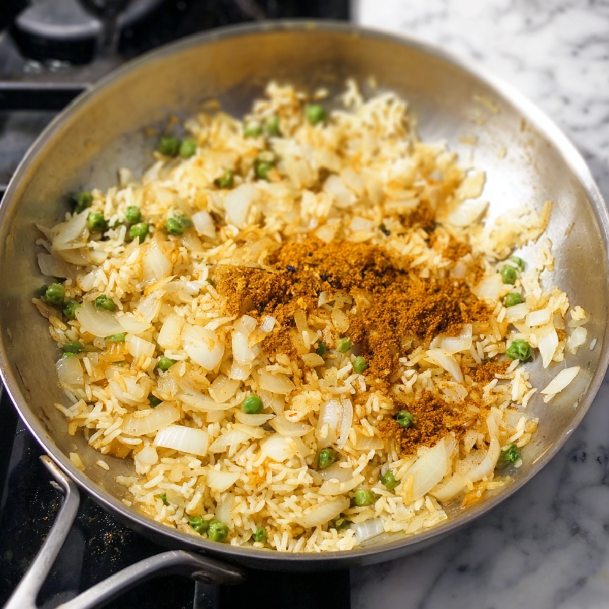 Healthy Turmeric Chicken and Rice Casserole 10 A skillet filled with rice, green peas, and sautéed onions. The rice appears to have absorbed the golden color from the turmeric, and a generous amount of spices is sprinkled on top, ready to be stirred into the mixture for a flavorful base.