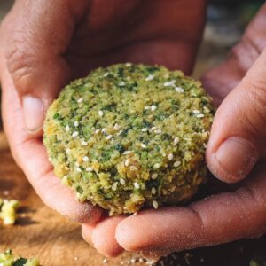 Easy Authentic Falafel Recipe | Golden & Crispy in 50 Min 17 Close-up of hands shaping raw falafel mixture into a round patty, green chickpea and herb mixture with sesame seeds visible