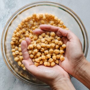 Easy Authentic Falafel Recipe | Golden & Crispy in 50 Min 15 Hands holding soaked chickpeas in a glass bowl filled with water, preparing chickpeas for homemade falafel
