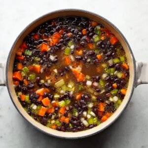 Easy Black Bean Soup Recipe - Ready in Just 30 Minutes 15 Top-down photo of a pot with black beans simmering in broth with diced carrots, celery, and onions, rustic homemade soup, clean white background, natural lighting