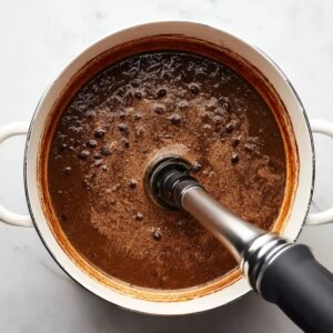 Easy Black Bean Soup Recipe - Ready in Just 30 Minutes 16 Overhead photo of black bean soup being blended with an immersion blender in a white pot, thick creamy texture, cooking in progress, white marble background, natural light