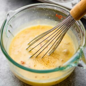 Healthy Breakfast Egg Muffins Recipe 15 A close-up of a glass measuring cup filled with egg mixture, whisked together with diced ham and seasoning, ready for baking.