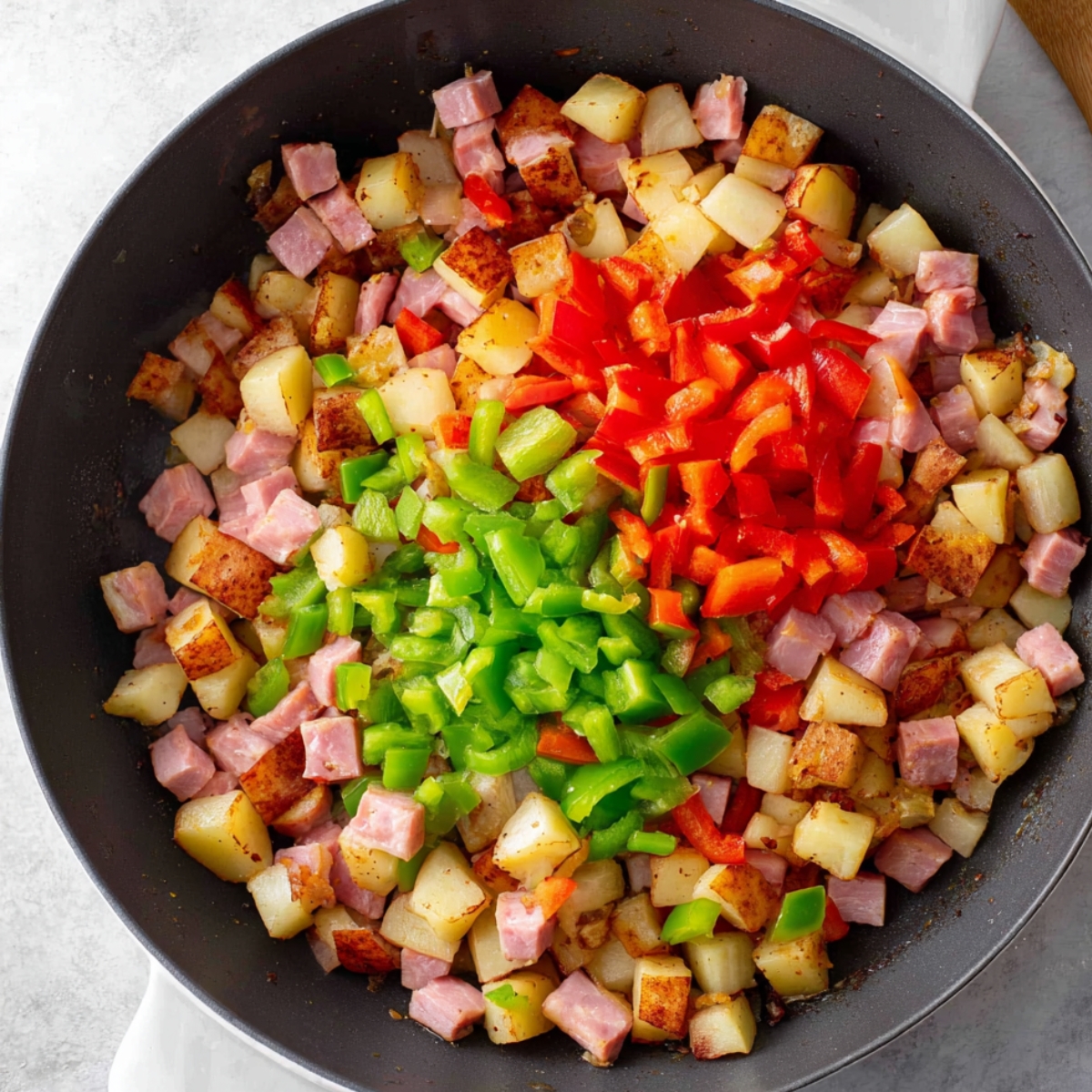 30-Minute Breakfast Skillet | Crispy Potatoes & Eggs 10 Skillet filled with diced potatoes, ham, red bell peppers, and green bell peppers layered before mixing for a breakfast hash.