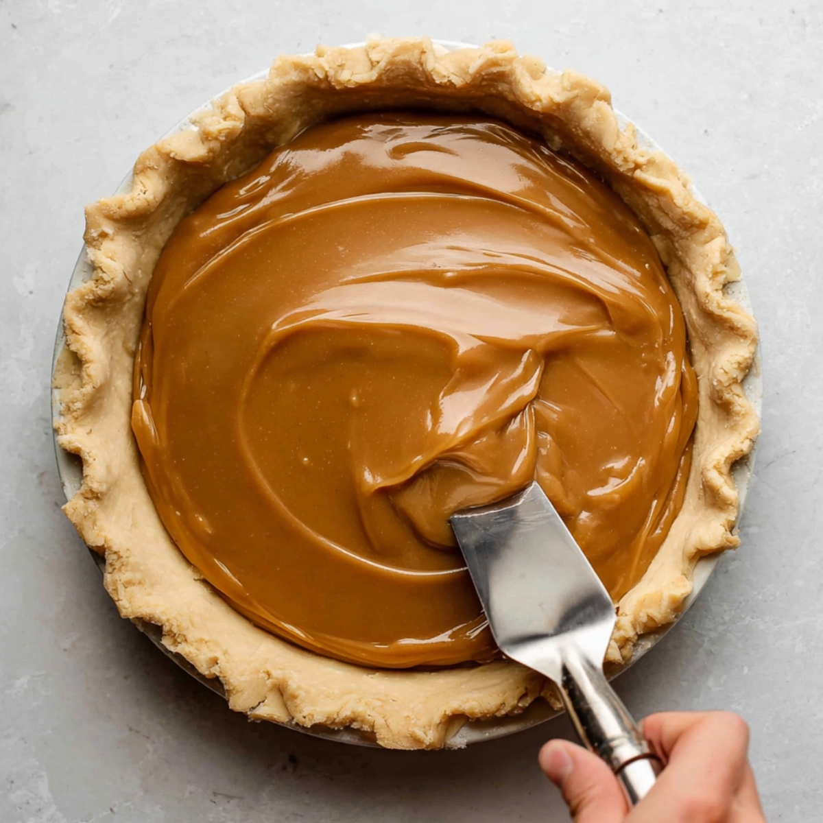 Easy Butterscotch Pie Recipe | 9 Steps to Silky Perfection 12 Smooth butterscotch filling being spread evenly into a baked pie crust with a spatula.
