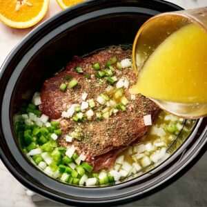 Carnitas Crockpot Recipe | 10 Ingredients, 8 Hours 16 Overhead shot of raw pork shoulder seasoned with spices inside a slow cooker, chopped onions and green peppers around the meat, orange juice being poured in, preparation stage of carnitas, clean modern kitchen, bright natural light, detailed realistic style