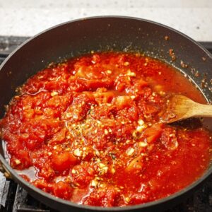Easy Creamy Tomato Gnocchi with Burrata Recipe 15 A pan filled with crushed tomatoes in a rich tomato sauce, with bits of garlic and spices cooking together