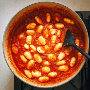 Easy Creamy Tomato Gnocchi with Burrata Recipe 16 A pot with gnocchi floating in a vibrant red tomato sauce, stirred with a black spatula