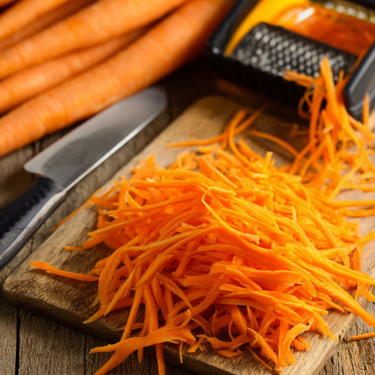Healthy Cucumber and Carrot Salad Recipe 11 Freshly julienned carrots on a wooden cutting board, next to a vegetable peeler and knife, prepared for an Asian-style salad.