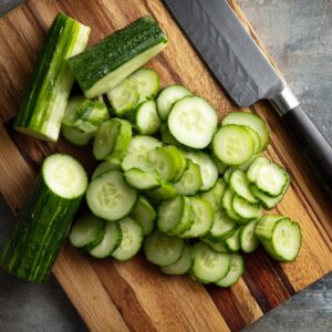 Healthy Cucumber and Carrot Salad Recipe 15 Sliced cucumbers on a wooden cutting board, with a sharp knife nearby, fresh and ready to be mixed into a vibrant salad