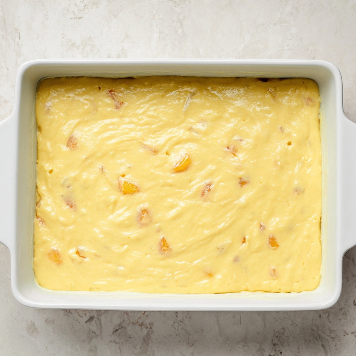 Brown Sugar Peach Cake Recipe | Easy & Moist 12 Rectangular white baking dish filled with pale yellow cake batter dotted with peach pieces, viewed from above.