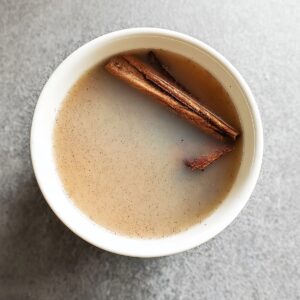 Authentic Horchata Recipe | Homemade Mexican Drink 16 “Top-down view of a white ceramic cup filled with light brown horchata, cinnamon sticks floating in the drink, subtle cloudy texture in the liquid, minimalist food photography, neutral gray stone countertop, soft natural lighting, realistic colors, high detail, shallow shadows, modern aesthetic, 4k resolution”