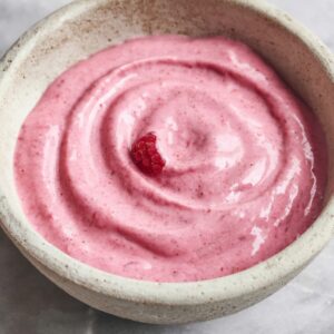 Creamy raspberry smoothie bowl in a rustic ceramic bowl on a marble countertop with a smooth pink texture.