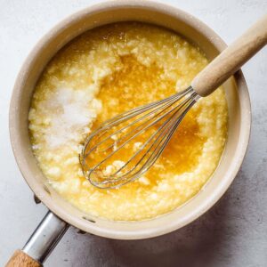 Healthy Rømmegrøt Recipe: Creamy Norwegian Porridge in 55 Minutes 16 Saucepan showing butter separating from a cooked mixture, with curds forming and a whisk stirring the mixture during cooking.