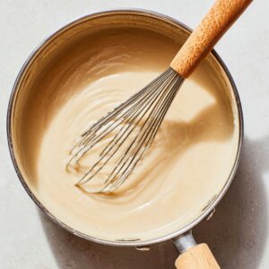 Healthy Rømmegrøt Recipe: Creamy Norwegian Porridge in 55 Minutes 17 Smooth creamy porridge being whisked in a saucepan, showing a thick and silky texture during the cooking process.