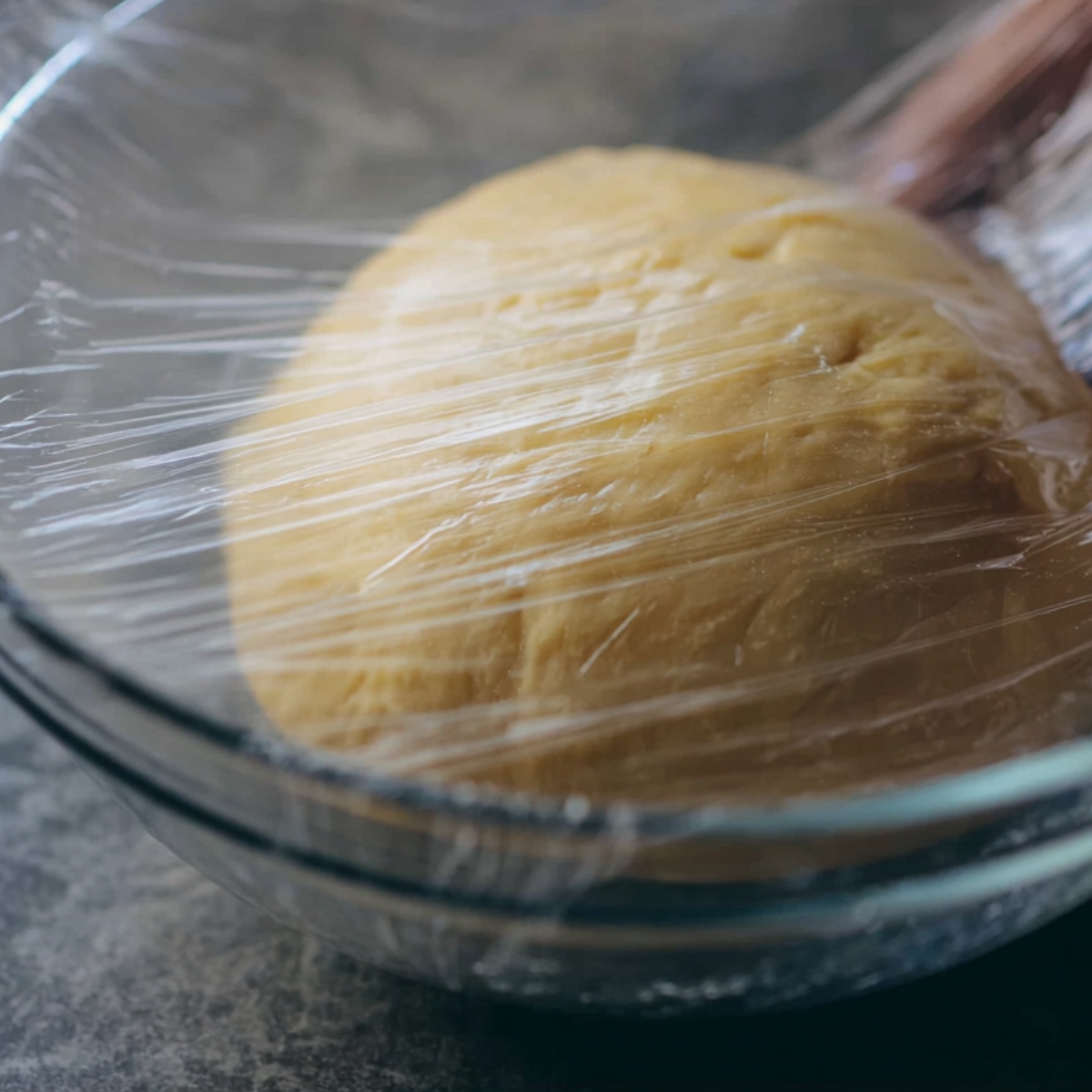 Struffoli Recipe Italian | Easy Honey-Coated Dough Balls 11 A smooth ball of dough resting in a glass bowl covered with plastic wrap, dough resting stage before shaping and frying.