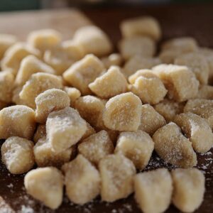 Struffoli Recipe Italian | Easy Honey-Coated Dough Balls 17 Raw struffoli dough pieces cut into small chunks and lightly dusted with flour on a wooden surface before frying.