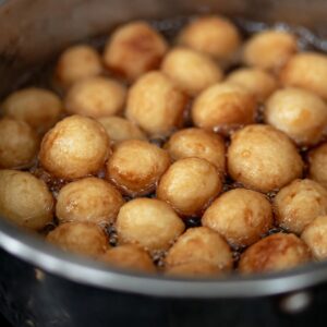 Struffoli Recipe Italian | Easy Honey-Coated Dough Balls 18 Small dough balls frying in hot oil inside a pan, turning golden brown and crispy, traditional Italian struffoli cooking process.