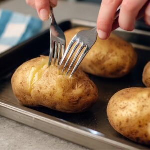 Taco Potatoes Recipe | Double Stuffed & Cheesy 15 Close-up food preparation photography of hands piercing whole russet potatoes with a fork on a baking tray, step-by-step recipe process, clean kitchen setup, natural lighting, realistic texture, instructional food photography