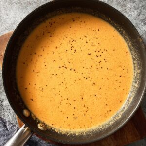 Creamy gravy base cooking in a skillet, light orange color with black pepper specks, top-down view.