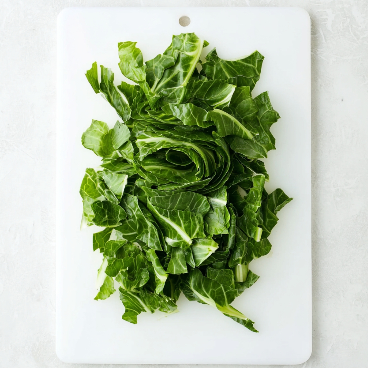 Best Turnip Greens Recipe - Smoked Turkey & Pot Liquor 11 Fresh collard greens sliced into thin ribbons on a white cutting board.