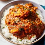 Achiote Chicken A bowl of tender chicken cooked in achiote sauce, served over a bed of fluffy white rice, garnished with fresh herbs