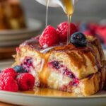 Berry Stuffed French Toast Close-up shot of a slice of berry stuffed French toast on a plate with maple syrup being poured over it, fresh raspberries and blueberries on top, golden crispy edges, creamy berry filling visible, warm natural lighting, shallow depth of field, high detail, food photography, breakfast scene