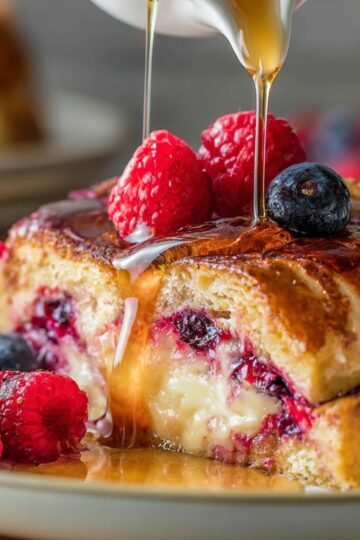 Easy Berry Stuffed French Toast Recipe 1 Berry Stuffed French Toast Close-up shot of a slice of berry stuffed French toast on a plate with maple syrup being poured over it, fresh raspberries and blueberries on top, golden crispy edges, creamy berry filling visible, warm natural lighting, shallow depth of field, high detail, food photography, breakfast scene
