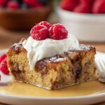 Bread Pudding A delicious slice of bread pudding served with a dollop of whipped cream and fresh raspberries on top, set on a white plate with a backdrop of berries and a cozy kitchen scene.