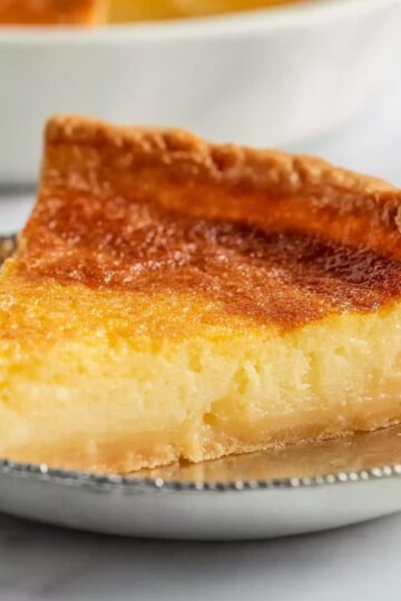 Best Buttermilk Pie Recipe 2 Buttermilk Pie A slice of buttermilk pie with a golden, flakey crust and smooth, custard-like filling. The pie is partially cut, revealing its creamy texture, and sits on the edge of a silver pie dish.