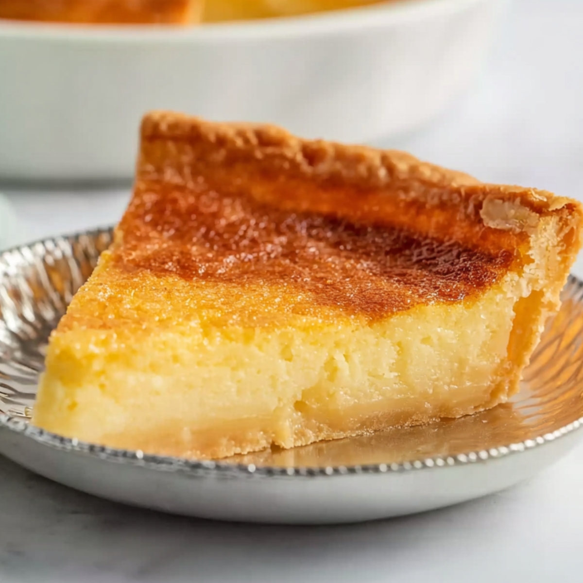 Best Buttermilk Pie Recipe 9 Buttermilk Pie A slice of buttermilk pie with a golden, flakey crust and smooth, custard-like filling. The pie is partially cut, revealing its creamy texture, and sits on the edge of a silver pie dish.