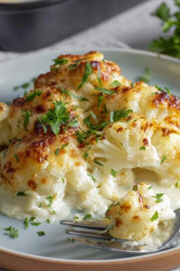 Best Cauliflower Gratin Recipe 1 Cauliflower Gratin A plate of freshly baked cauliflower gratin, featuring golden-brown, cheesy, and creamy florets with a crispy top. The dish is garnished with freshly chopped parsley and served with a fork on the side.
